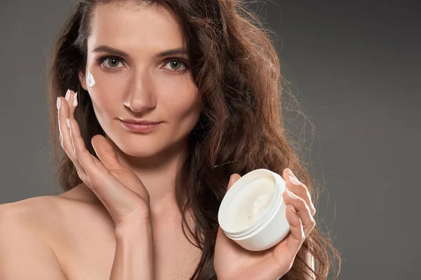 Hermosa mujer aplicando crema hidratante para la cara, aislado en gris - foto de stock