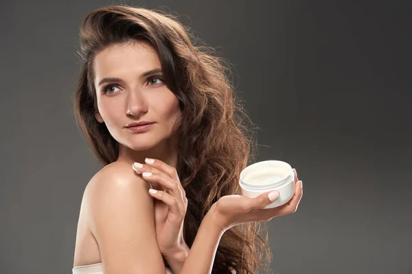 Young tender woman applying moisturizing face cream, isolated on grey — Stock Photo