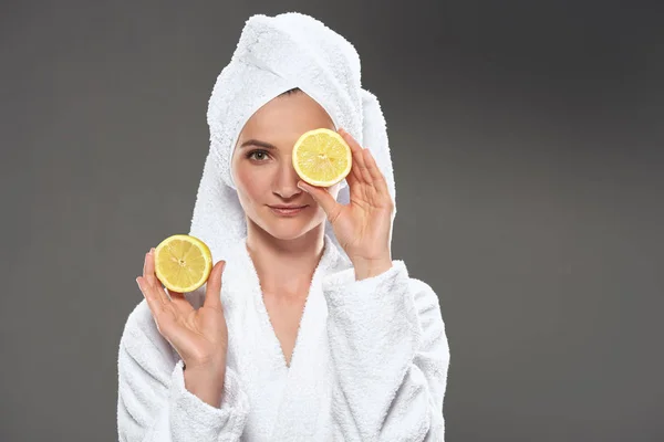 Elegant girl with lemon slices in white bathrobe and towel, isolated on grey — Stock Photo