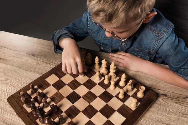 Vue surélevée du petit garçon à lunettes jouant aux échecs à table — Photo de stock