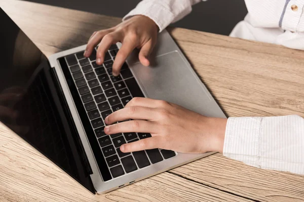 Imagen recortada de colegial haciendo tarea en el ordenador portátil con pantalla en blanco en la mesa - foto de stock