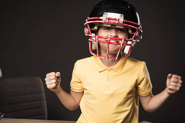 Улыбающийся маленький мальчик в защитном шлеме для американского футбола жестикулируя руками на сером фоне — стоковое фото