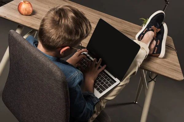Rear view of little boy with legs on table using laptop with blank screen on grey background — Stock Photo