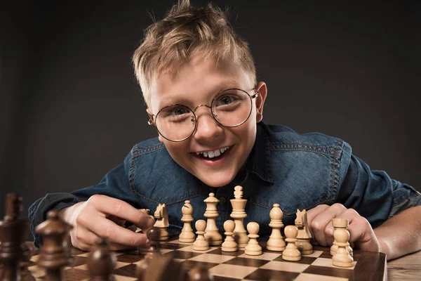 Niño sonriente en anteojos jugando ajedrez aislado sobre fondo gris - foto de stock