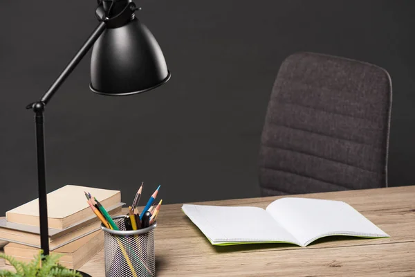 Foco selectivo de la lámpara, lápices de color, pila de libros, planta y libro de texto vacío sobre la mesa sobre fondo gris - foto de stock