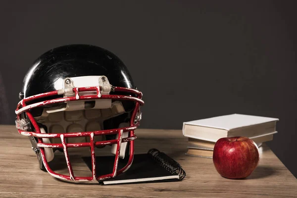 Vista ravvicinata di casco da calcio americano, libro di testo, mela e pila di libri su sfondo grigio — Foto stock