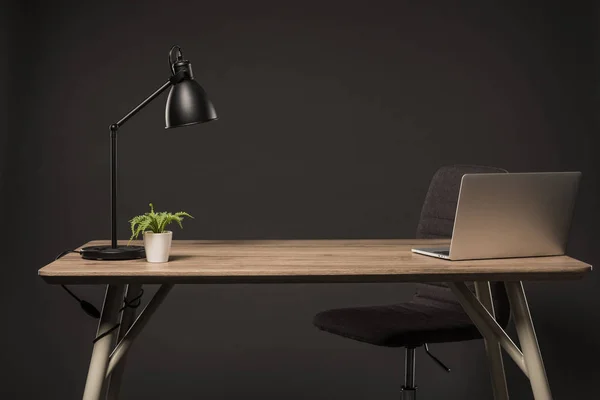 Vista de cerca de la silla y la mesa con lámpara, planta, libro y portátil sobre fondo gris - foto de stock