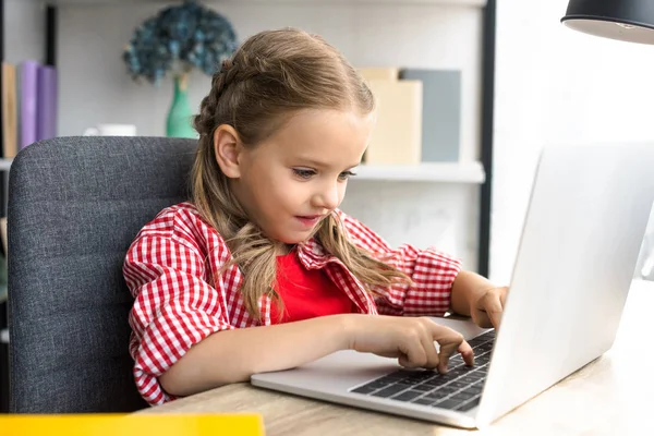 Вид сбоку маленького ребенка, использующего ноутбук за столом дома — Stock Photo