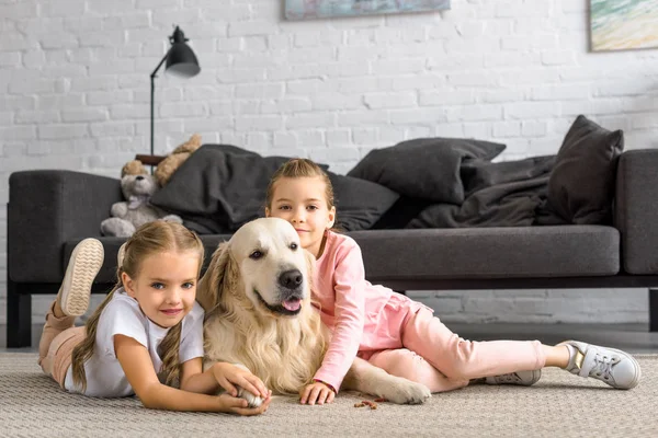 Adorável crianças abraçando golden retriever cão enquanto sentado no chão em casa — Fotografia de Stock