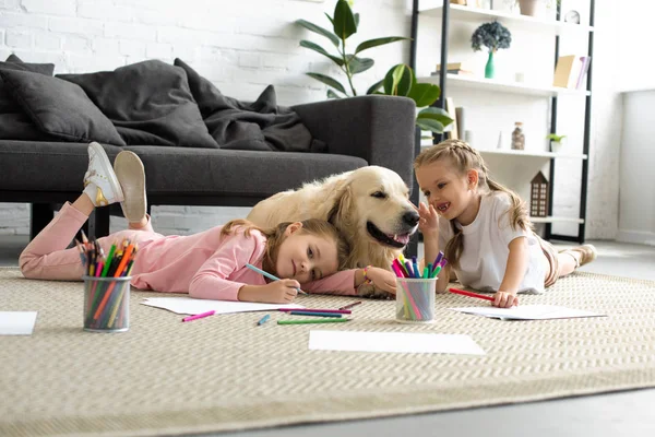 Sonrientes niños acostados en el suelo junto con perro golden retriever en casa - foto de stock