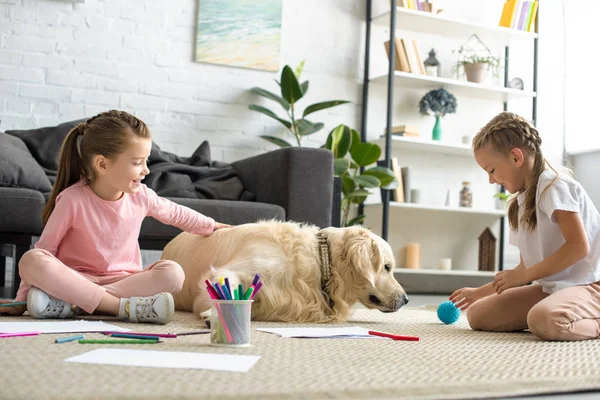 Little children playing with golden retriever dog on floor at home — Stock Photo