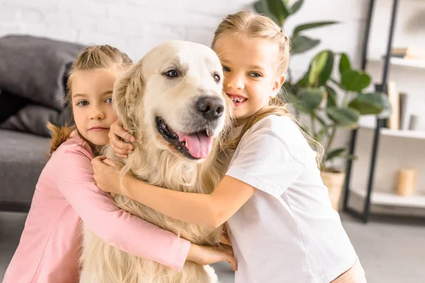 Portrait of adorable smiling kids hugging golden retriever dog at home — Stock Photo