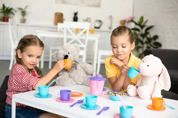 Adorables hermanitas fingiendo tener una fiesta de té juntas en casa - foto de stock