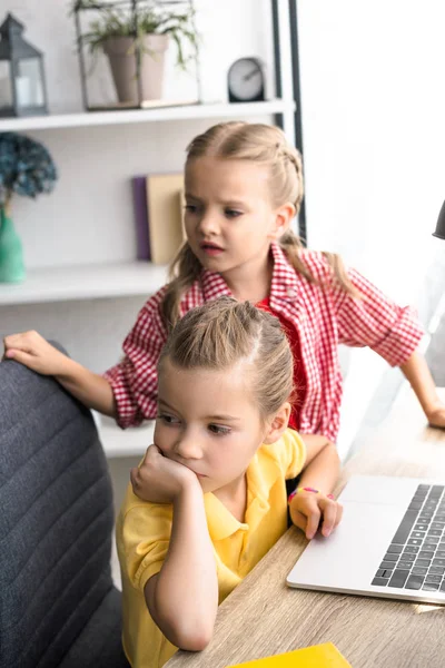 Messa a fuoco selettiva dei bambini piccoli che guardano lontano a tavola con il computer portatile a casa — Foto stock