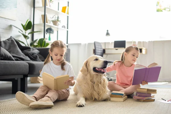 Monas hermanitas leyendo libros con perro golden retriever cerca de casa - foto de stock