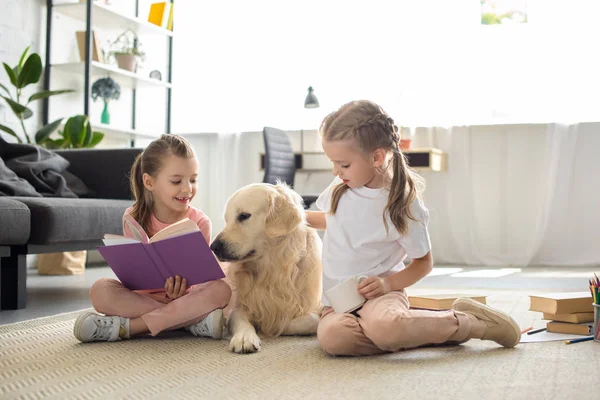 Irmãzinhas com livros e cão golden retriever perto de sentar no chão em casa — Fotografia de Stock