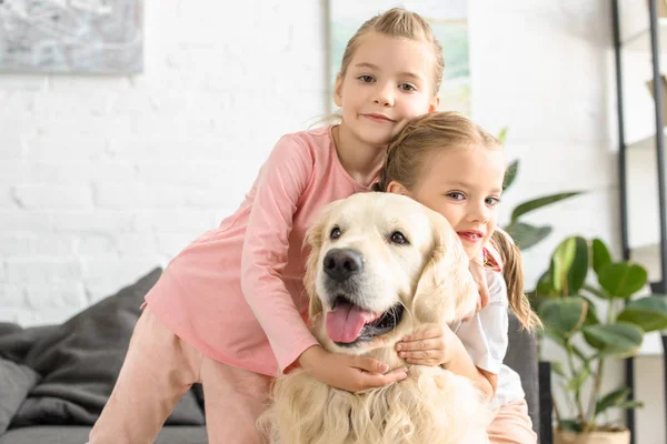 Retrato de niños adorables abrazando perro golden retriever en casa - foto de stock