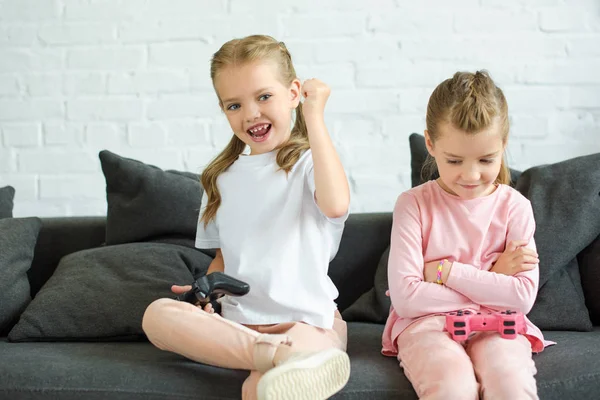 Adorable little sisters with gamepads playing video game together at home — Stock Photo