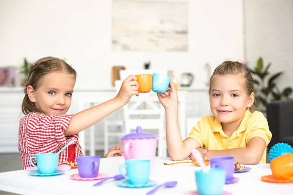 Monas hermanas pequeñas tazas de juguete tintineo mientras fingen tener fiesta de té juntos en casa - foto de stock