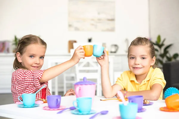 Cute little sisters clinking toy cups while pretending to have tea party together at home — Stock Photo