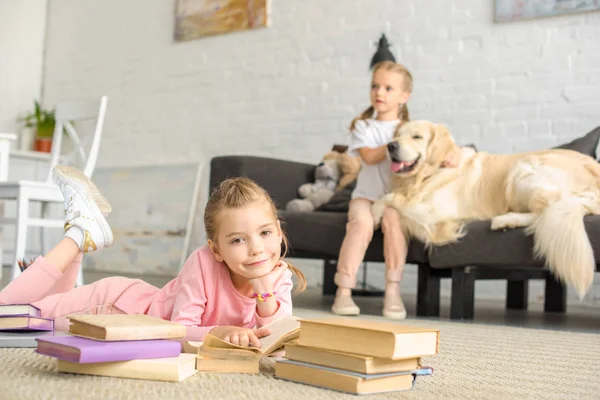 Enfoque selectivo de hermanas pequeñas con libros y perro golden retriever cerca en casa - foto de stock