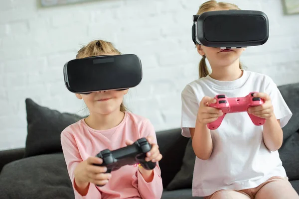 Скрытый вид детей в наушниках виртуальной реальности, играющих в видеоигры на диване дома — стоковое фото