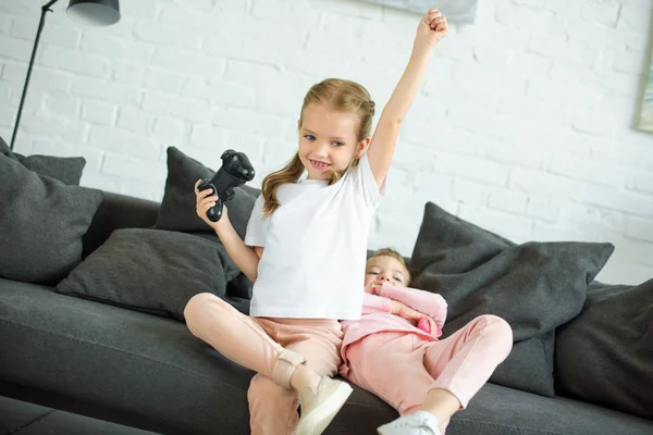 Милые маленькие сестры с геймпадами, играющие вместе в видеоигры дома — стоковое фото