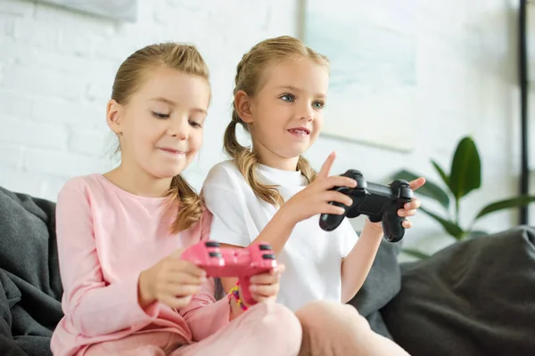 Retrato de hermanas pequeñas con gamepads jugando videojuego juntas en casa - foto de stock