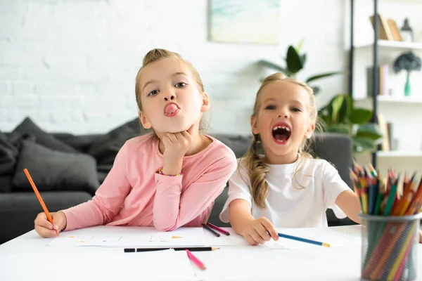 Portrait of adorable sisters grimacing while drawing pictures at home — Stock Photo