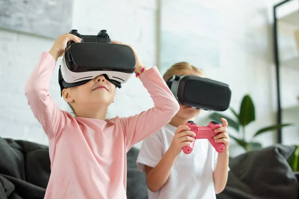 Obscured view of kids in virtual reality headsets playing video game on sofa at home — Stock Photo