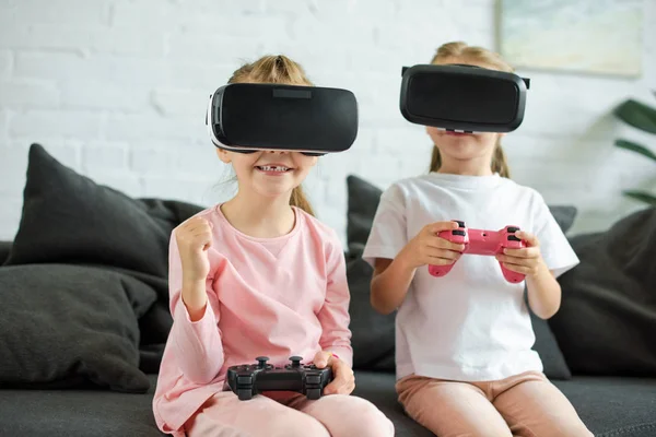 Visión oscura de los niños en auriculares de realidad virtual jugando videojuego en el sofá en casa - foto de stock