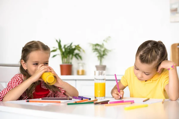 Lindos niños pequeños dibujando imágenes en la mesa en casa - foto de stock