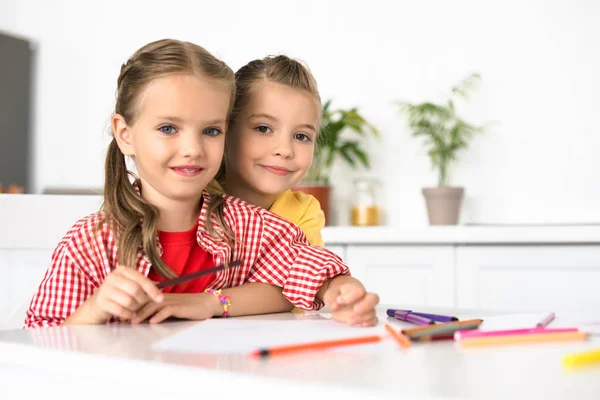 Портрет милых маленьких детей за столом с бумагами и карандашами для рисования дома — стоковое фото