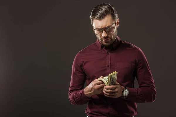 Homem sério em óculos contando notas de dólar isoladas em preto — Fotografia de Stock