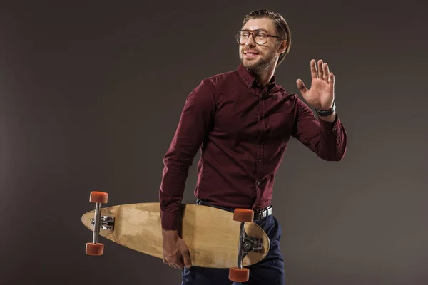 Schöner lächelnder Mann mit Brille, Longboard haltend und isoliert auf schwarz wegschauend — Stockfoto