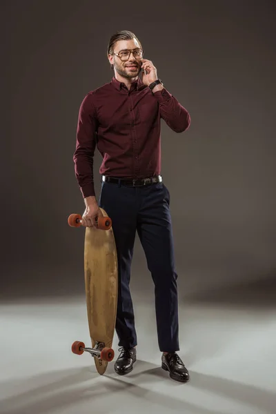 Усміхнений чоловік тримає скейтборд і розмовляє по смартфону на чорному — стокове фото