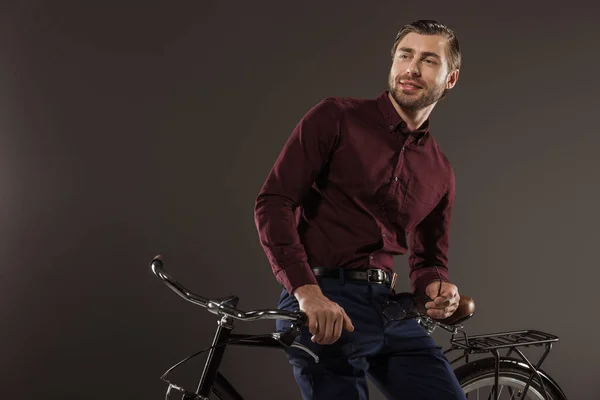 Schöner lächelnder junger Mann sitzt auf einem Fahrrad und schaut weg auf schwarz — Stock Photo