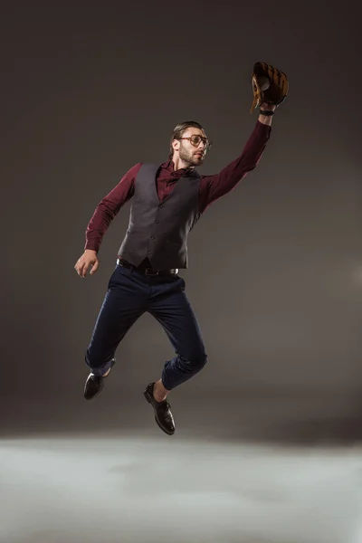 Joven hombre de negocios en el guante de béisbol saltando y la captura de la bola en negro - foto de stock