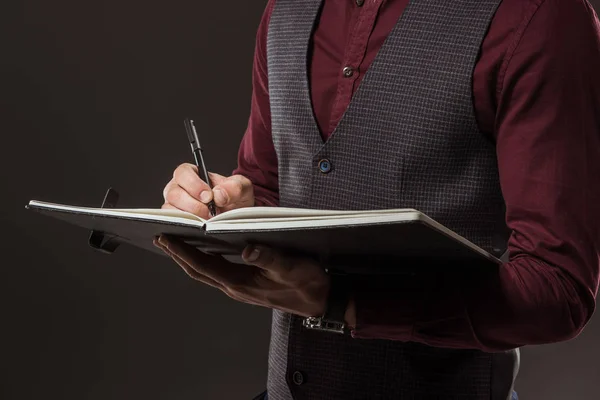 Cropped shot of businessman taking notes in notepad isolated on black — Stock Photo