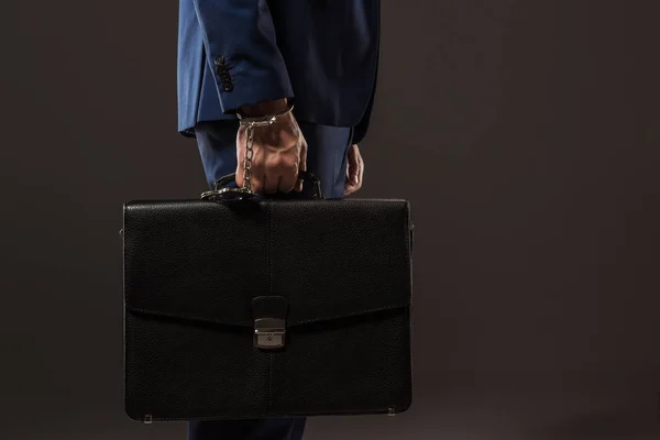 Side view of businessman in handcuffs holding briefcase isolated on black — Stock Photo