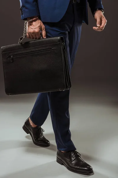 Cropped shot of businessman in handcuffs with briefcase on black — Stock Photo