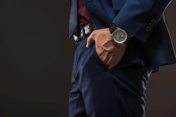 Cropped shot of businessman with wristwatch standing with hand in pocket isolated on black — Stock Photo