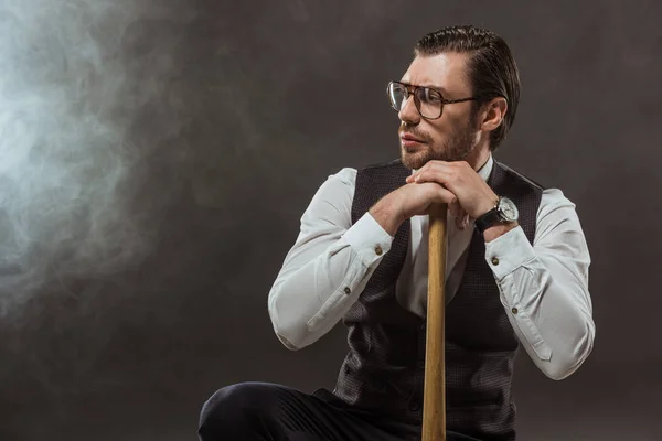 Ernster, stylischer Mann mit Brille, Baseballschläger in der Hand und wegschauend auf schwarz — Stockfoto