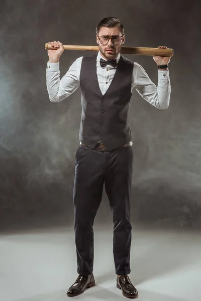 Full length view of handsome serious man holding baseball bat and looking at camera while standing in smoke — Stock Photo