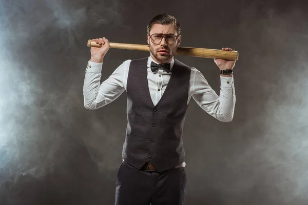 Handsome serious man holding baseball bat and looking at camera while standing in smoke — Stock Photo