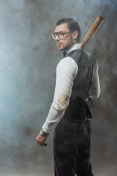 Schöner Mann mit Fliege und Brille hält Baseballschläger in der Hand und schaut im Rauch weg — Stockfoto