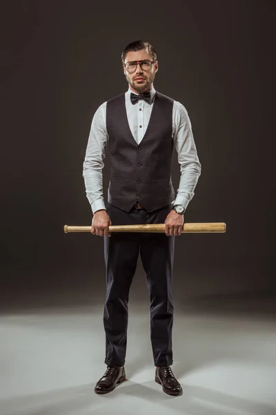 Full length view of stylish man in bow tie and eyeglasses holding baseball bat and looking at camera on black — Stock Photo