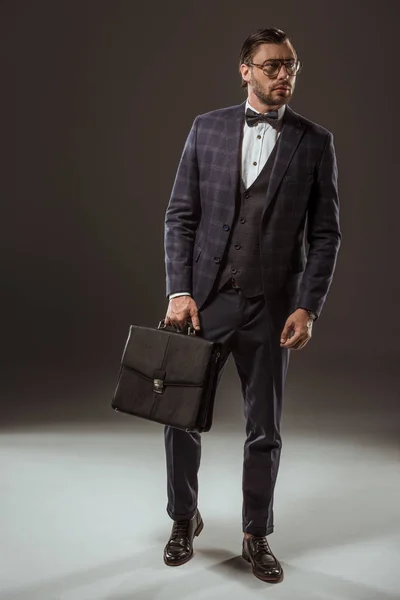 Вид бизнесмена в полный рост, держащего чемодан и отводящего вдаль взгляд на черный — стоковое фото