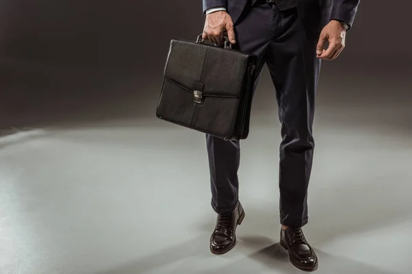 Низкая секция бизнесмена в формальной одежде, держащего портфель на черном — стоковое фото