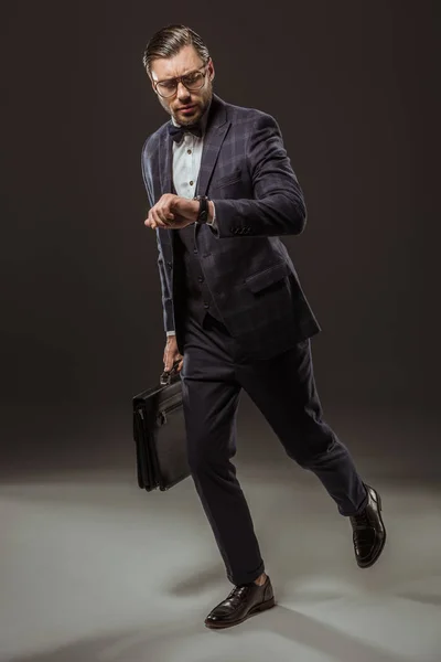 Seriöser Geschäftsmann mit Aktentasche, die Armbanduhr überprüft und auf schwarz läuft — Stockfoto